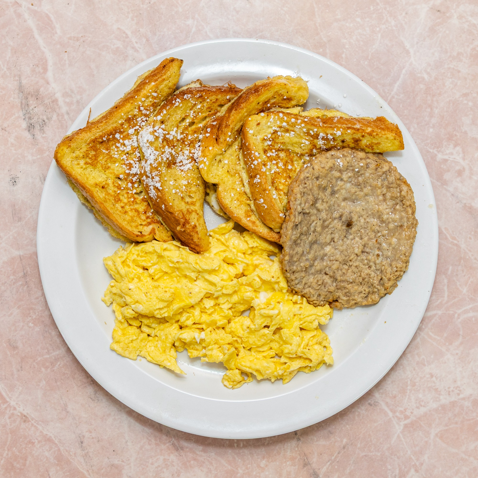 Breakfast plate with powdered sugar French toast, scrambled eggs, and a sausage patty.
