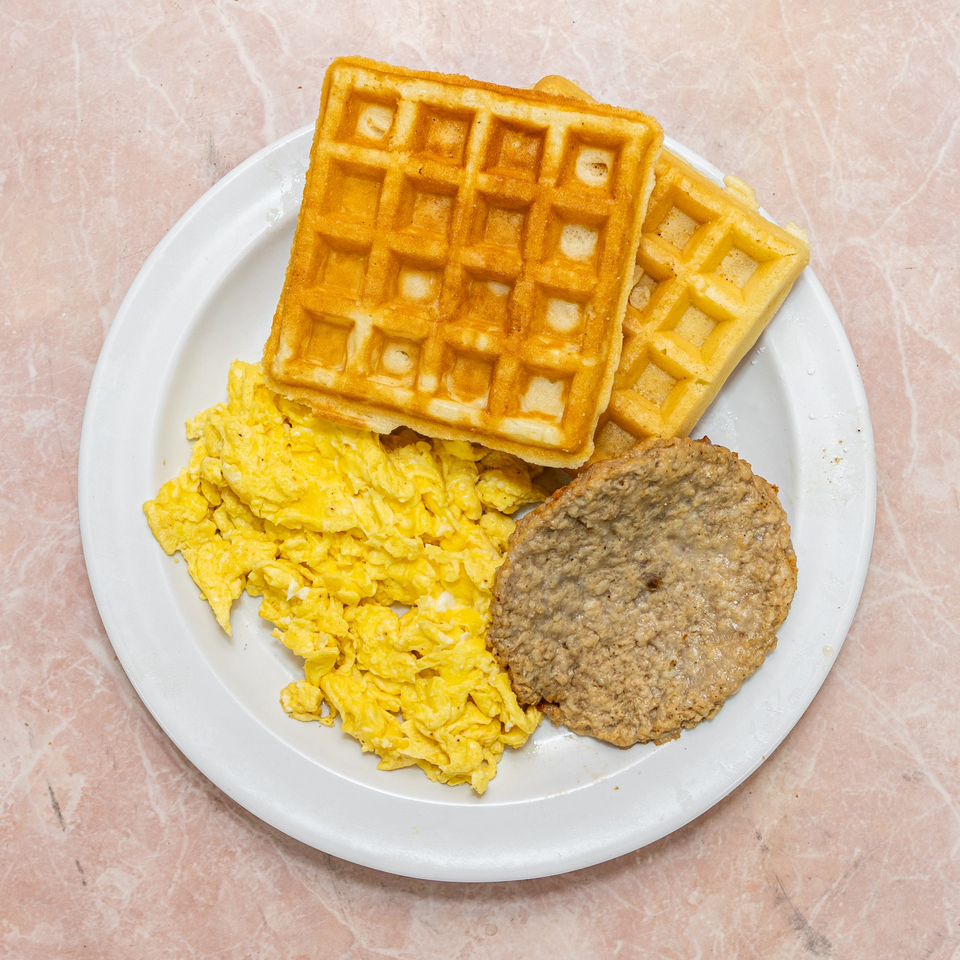 A breakfast plate with two golden waffles, fluffy scrambled eggs, and a sausage patty.