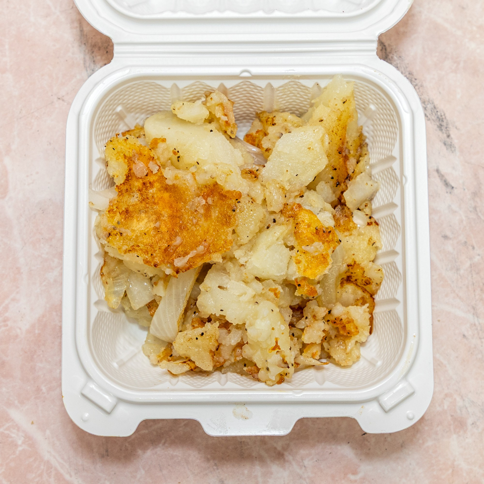 Golden brown fried potatoes and onions in a white takeout container.